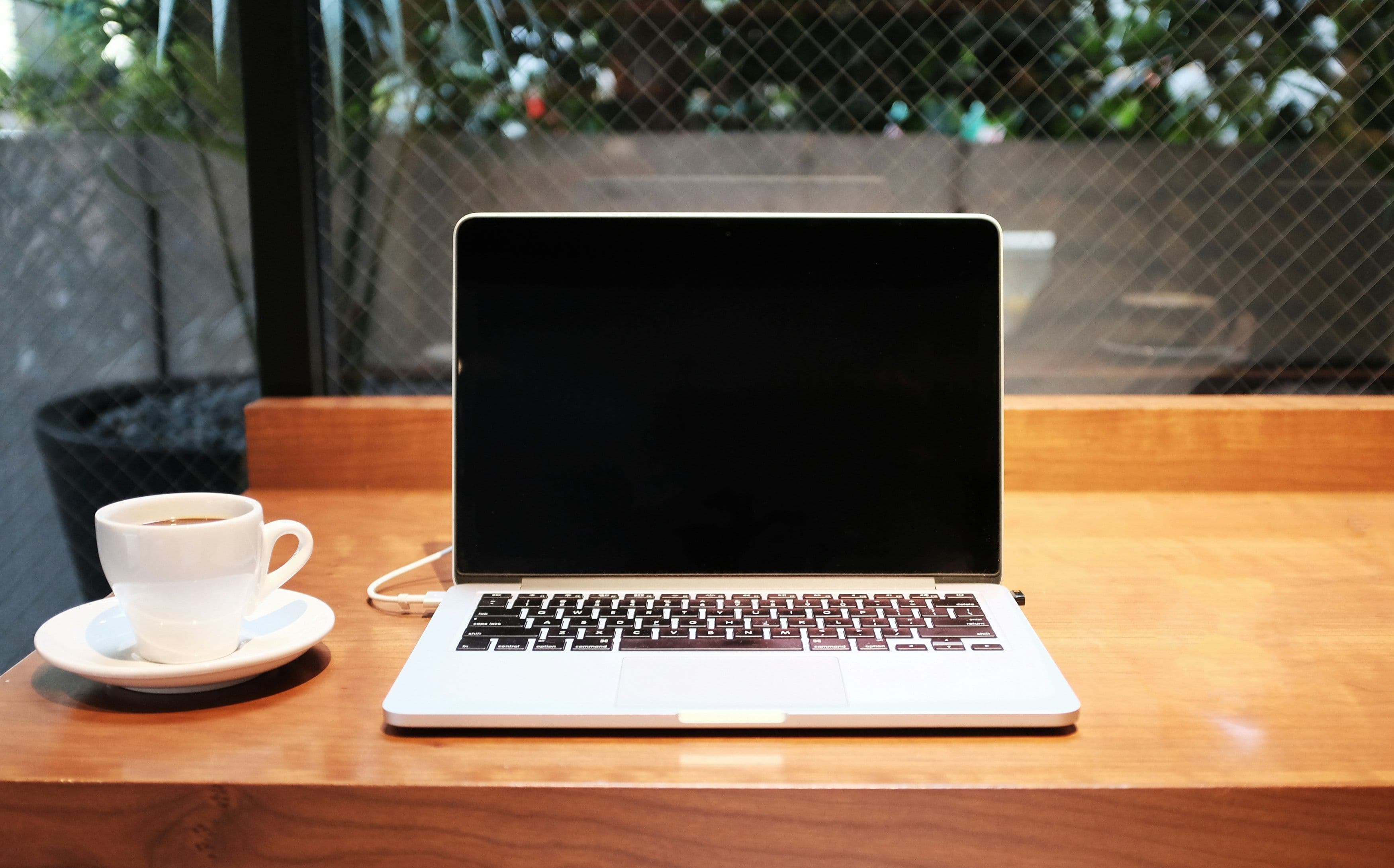 Laptop auf einem Holztisch mit einer Tasse Kaffee daneben, bereit für Online-Arbeit