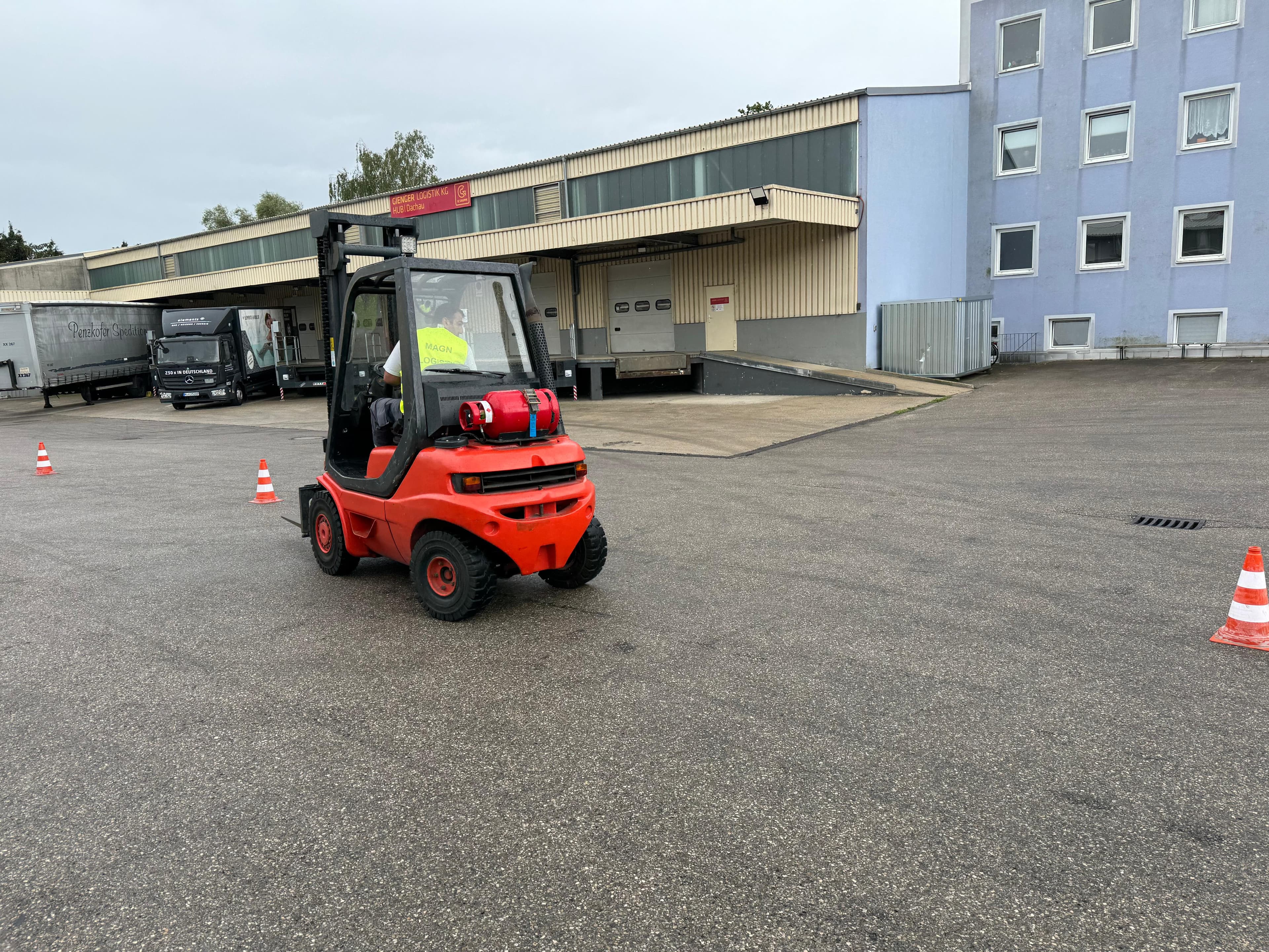 Gabelstaplerfahrer manövriert einen roten Stapler durch einen Übungsparcours mit Verkehrskegeln.